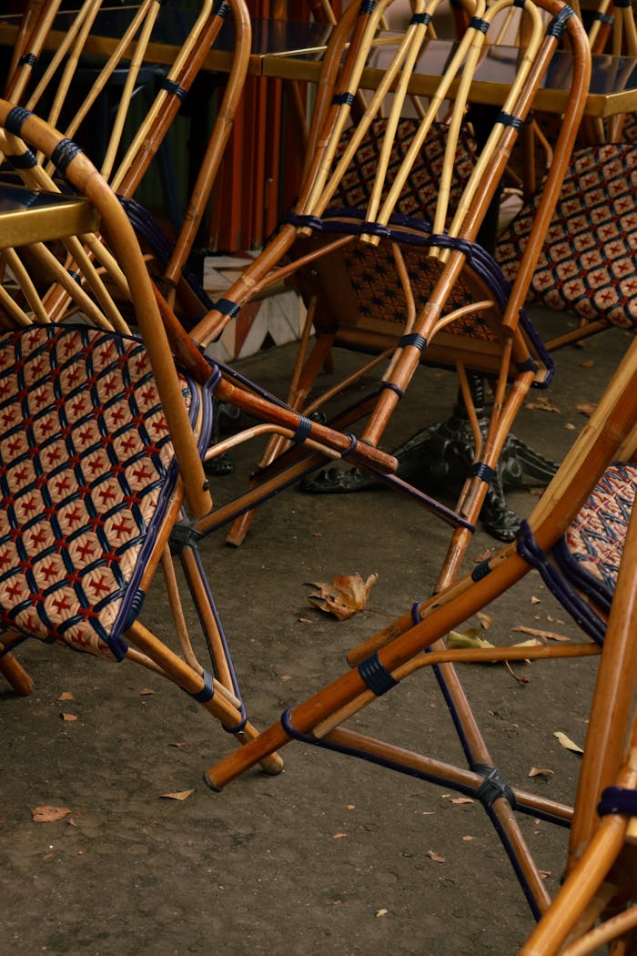 A stack of patterned wooden bistro chairs neatly arranged outside a cafe, suggesting a quiet moment.